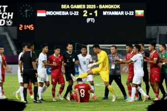 Insiden tak terpuji mewarnai pertandingan sepak bola putra SEA Games 2025 antara Timnas Indonesia U-22 dan Timnas Myanmar U-22, Jumat (13/12/2025). Laga yang berlangsung di 700th Anniversary Stadium, Chiang Mai, Thailand, itu berjalan dalam tensi tinggi. Skuad Merah Putih tampil ngotot karena membutuhkan kemenangan besar demi menjaga peluang lolos ke semifinal. Peluit Panjang Picu Keributan Intensitas pertandingan meningkat tajam menjelang laga berakhir. Puncaknya terjadi saat wasit meniup peluit panjang setelah bola keluar lapangan, menandai berakhirnya pertandingan. Keputusan tersebut memicu protes keras dari sejumlah pemain Indonesia. Ivar Jenner dan Zanadin Fariz diganjar kartu kuning akibat aksi protes. Situasi kian memanas ketika Zanadin harus menerima kartu merah, lantaran sebelumnya sudah mengoleksi satu kartu kuning. Kiper Myanmar Tendang Dion Markx Setelah kartu merah dikeluarkan, beberapa pemain Timnas Indonesia U-22 kembali mendekati wasit untuk mempertanyakan keputusannya. Protes juga datang dari pemain pengganti yang mengenakan rompi biru muda dan sempat merangsek masuk ke lapangan dari area bangku cadangan. Dalam situasi tersebut, bek Timnas Indonesia U-22 Kadek Arel terlihat berlari menuju tengah lapangan. Ia berupaya menarik Dion Markx, yang sedang terlibat adu mulut dengan pemain Myanmar. Meski sempat dilerai, Dion kembali terlibat friksi dengan penjaga gawang lawan. Aksi saling dorong pun tak terhindarkan hingga akhirnya kiper cadangan Myanmar U-22 melayangkan tendangan ke arah Dion Markx. Aksi tersebut menjadi pemicu utama kericuhan besar di tengah lapangan. Sejumlah pemain dari kedua tim langsung berusaha melerai agar situasi tidak semakin meluas. Indra Sjafri dan Sumardji Turun Tangan Para pemain Indonesia dan Myanmar tampak berupaya menenangkan keadaan. Dion Markx ditarik dan diredam oleh rekan-rekannya, sementara kiper Myanmar U-22 Khant Min Thant yang terlihat emosional juga segera dilerai oleh sesama pemain. Tak hanya pemain, jajaran ofisial dan tim pelatih dari kedua kubu turut turun ke lapangan. Pelatih Timnas Indonesia U-22 Indra Sjafri, bersama para asistennya seperti Bima Sakti dan Zulkifli Syukur, serta manajer tim Sumardji, terlihat aktif menenangkan situasi. Situasi Berhasil Dikendalikan Beruntung, kericuhan dan adu fisik tersebut tidak berkembang lebih jauh. Ofisial kedua tim meminta para pemain untuk segera meninggalkan lapangan dan kembali ke bangku cadangan masing-masing. Pertandingan pun akhirnya benar-benar berakhir tanpa insiden lanjutan, meski meninggalkan catatan kelam akibat kericuhan usai peluit panjang.