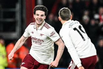 Arsenal menang dengan cukup dramatis saat berduel lawan Bournemouth di pekan ke-20 Liga Inggris 2025/2026 di Vitality Stadium, Minggu (04/01/2026). Bournemouth membuat kejutan saat Evanilson bisa mencetak gol lebih dahulu. Ia memanfaatkan blunder Gabriel Magalhaes. Namun bek asal Brasil itu menebus kesalahannya dan membuat skor berimbang 1-1. Setelah itu Declan Rice mencetak dua gol dan membuat Arsenal dalam posisi unggul 1-3. Bournemouth sempat mencetak satu gol lagi melalui tembakan keras Eli Junior Kroupi. Namun Arsenal akhirnya bisa mengamankan kemenangan dengan skor 2-3. Berikut rapor pemain Arsenal di pertandingan tersebut. Rapor Pemain Belakang dan Kiper David Raya: 6 Kiper asal Spanyol itu praktis tak punya banyak pilihan saat gol pembuka tercipta. Sepakan Kroupi terlalu cepat dan sulit dijangkau, meski Raya nyaris bereaksi dengan penyelamatan refleks. Jurrien Timber: 7.5 Timber tampil sigap dengan tekel krusial di dekat garis gawang yang langsung berujung serangan balik. Ia juga melakukan intervensi terakhir yang sempurna untuk menggagalkan peluang emas David Brooks. William Saliba: 6.5 Bek Prancis ini tidak bisa berbuat banyak pada momen gol Bournemouth. Namun, ia tetap tenang dan cukup solid saat menghadapi tekanan tuan rumah sepanjang laga. Gabriel Magalhaes: 7 Awal laga menjadi mimpi buruk bagi Gabriel setelah kesalahan umpannya berujung gol gratis untuk Evanilson. Ia menebusnya dengan sempurna lewat gol yang menghidupkan kembali Arsenal. Piero Hincapie: 6 Dipercaya mengisi posisi bek kiri, Hincapie beberapa kali kerepotan menghadapi kecepatan Semenyo. Ia cukup sering kalah duel hingga peluit akhir berbunyi. Rapor Pemain Tengah Martin Zubimendi: 6 Zubimendi sempat kehilangan bola di awal pertandingan sebelum perlahan menemukan ritmenya. Kartu kuning membuatnya harus bermain ekstra hati-hati hingga akhir laga. Declan Rice: 9 Meski absen di laga tengah pekan, Rice langsung dipercaya sebagai starter di pantai selatan. Ia menjadi pembeda lewat dua gol krusial, termasuk sepakan rendah yang mematikan. Martin Odegaard: 8 Kapten Arsenal ini aktif mencari ruang di antara lini lawan, meski Bournemouth tampil disiplin. Satu assist yang ia ciptakan dan keterlibatannya dalam gol ketiga Arsenal kembali menegaskan pengaruh besarnya dalam permainan tim. Rapor Pemain Depan Noni Madueke: 7 Madueke menyia-nyiakan peluang emas di awal laga dengan tembakan yang melambung. Namun, pergerakannya dari sisi kanan berperan penting dalam terciptanya gol penyeimbang. Viktor Gyokeres: 5 Penyerang bernomor punggung 14 itu kembali kesulitan memberi ancaman berarti di lini depan. Selain kontribusi fisik saat proses gol, ia nyaris tak terlihat sepanjang pertandingan. Gabriel Martinelli: 7 Martinelli kerap unggul duel melawan Alex Jimenez di sisi kiri. Sayangnya, akurasi umpan akhirnya belum maksimal meski kontribusi udaranya krusial dalam build-up gol kedua. Rapor Pemain Pengganti Gabriel Jesus: 6 Jesus tampil sebagai pengganti Gyokeres pada menit ke-67 dan memberi dinamika berbeda di lini serang. Ia hampir mencetak gol lewat tembakan telat yang masih bisa ditepis Petrovic. Leandro Trossard: 6 Masuk menggantikan Martinelli pada menit ke-67, Trossard langsung memberi energi tambahan. Ia sempat menciptakan beberapa situasi berbahaya meski belum berbuah gol. Bukayo Saka: 7.5 Saka langsung memberi dampak instan usai masuk dari bangku cadangan usai menggantikan Madueke pada menit ke-67. Assist cerdasnya membantu Rice menuntaskan gol ketiga Arsenal. Mikel Merino: 6 Merino menggantikan Odegaard di menit ke-80. Ia sempat mencoba peruntungan lewat tembakan jarak jauh yang masih mampu diamankan kiper lawan.