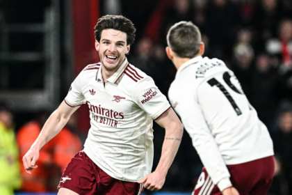 Arsenal menang dengan cukup dramatis saat berduel lawan Bournemouth di pekan ke-20 Liga Inggris 2025/2026 di Vitality Stadium, Minggu (04/01/2026). Bournemouth membuat kejutan saat Evanilson bisa mencetak gol lebih dahulu. Ia memanfaatkan blunder Gabriel Magalhaes. Namun bek asal Brasil itu menebus kesalahannya dan membuat skor berimbang 1-1. Setelah itu Declan Rice mencetak dua gol dan membuat Arsenal dalam posisi unggul 1-3. Bournemouth sempat mencetak satu gol lagi melalui tembakan keras Eli Junior Kroupi. Namun Arsenal akhirnya bisa mengamankan kemenangan dengan skor 2-3. Berikut rapor pemain Arsenal di pertandingan tersebut. Rapor Pemain Belakang dan Kiper David Raya: 6 Kiper asal Spanyol itu praktis tak punya banyak pilihan saat gol pembuka tercipta. Sepakan Kroupi terlalu cepat dan sulit dijangkau, meski Raya nyaris bereaksi dengan penyelamatan refleks. Jurrien Timber: 7.5 Timber tampil sigap dengan tekel krusial di dekat garis gawang yang langsung berujung serangan balik. Ia juga melakukan intervensi terakhir yang sempurna untuk menggagalkan peluang emas David Brooks. William Saliba: 6.5 Bek Prancis ini tidak bisa berbuat banyak pada momen gol Bournemouth. Namun, ia tetap tenang dan cukup solid saat menghadapi tekanan tuan rumah sepanjang laga. Gabriel Magalhaes: 7 Awal laga menjadi mimpi buruk bagi Gabriel setelah kesalahan umpannya berujung gol gratis untuk Evanilson. Ia menebusnya dengan sempurna lewat gol yang menghidupkan kembali Arsenal. Piero Hincapie: 6 Dipercaya mengisi posisi bek kiri, Hincapie beberapa kali kerepotan menghadapi kecepatan Semenyo. Ia cukup sering kalah duel hingga peluit akhir berbunyi. Rapor Pemain Tengah Martin Zubimendi: 6 Zubimendi sempat kehilangan bola di awal pertandingan sebelum perlahan menemukan ritmenya. Kartu kuning membuatnya harus bermain ekstra hati-hati hingga akhir laga. Declan Rice: 9 Meski absen di laga tengah pekan, Rice langsung dipercaya sebagai starter di pantai selatan. Ia menjadi pembeda lewat dua gol krusial, termasuk sepakan rendah yang mematikan. Martin Odegaard: 8 Kapten Arsenal ini aktif mencari ruang di antara lini lawan, meski Bournemouth tampil disiplin. Satu assist yang ia ciptakan dan keterlibatannya dalam gol ketiga Arsenal kembali menegaskan pengaruh besarnya dalam permainan tim. Rapor Pemain Depan Noni Madueke: 7 Madueke menyia-nyiakan peluang emas di awal laga dengan tembakan yang melambung. Namun, pergerakannya dari sisi kanan berperan penting dalam terciptanya gol penyeimbang. Viktor Gyokeres: 5 Penyerang bernomor punggung 14 itu kembali kesulitan memberi ancaman berarti di lini depan. Selain kontribusi fisik saat proses gol, ia nyaris tak terlihat sepanjang pertandingan. Gabriel Martinelli: 7 Martinelli kerap unggul duel melawan Alex Jimenez di sisi kiri. Sayangnya, akurasi umpan akhirnya belum maksimal meski kontribusi udaranya krusial dalam build-up gol kedua. Rapor Pemain Pengganti Gabriel Jesus: 6 Jesus tampil sebagai pengganti Gyokeres pada menit ke-67 dan memberi dinamika berbeda di lini serang. Ia hampir mencetak gol lewat tembakan telat yang masih bisa ditepis Petrovic. Leandro Trossard: 6 Masuk menggantikan Martinelli pada menit ke-67, Trossard langsung memberi energi tambahan. Ia sempat menciptakan beberapa situasi berbahaya meski belum berbuah gol. Bukayo Saka: 7.5 Saka langsung memberi dampak instan usai masuk dari bangku cadangan usai menggantikan Madueke pada menit ke-67. Assist cerdasnya membantu Rice menuntaskan gol ketiga Arsenal. Mikel Merino: 6 Merino menggantikan Odegaard di menit ke-80. Ia sempat mencoba peruntungan lewat tembakan jarak jauh yang masih mampu diamankan kiper lawan.